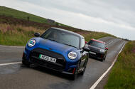 A black and red MINI John Cooper Works Aceman follows a blue and black MINI John Cooper Works Electric down a long straight country road in the peak district