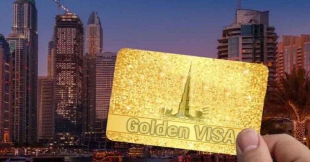 Shows a hand holding a golden card with Golden visa written on it, and UAE skyscrapers in the background